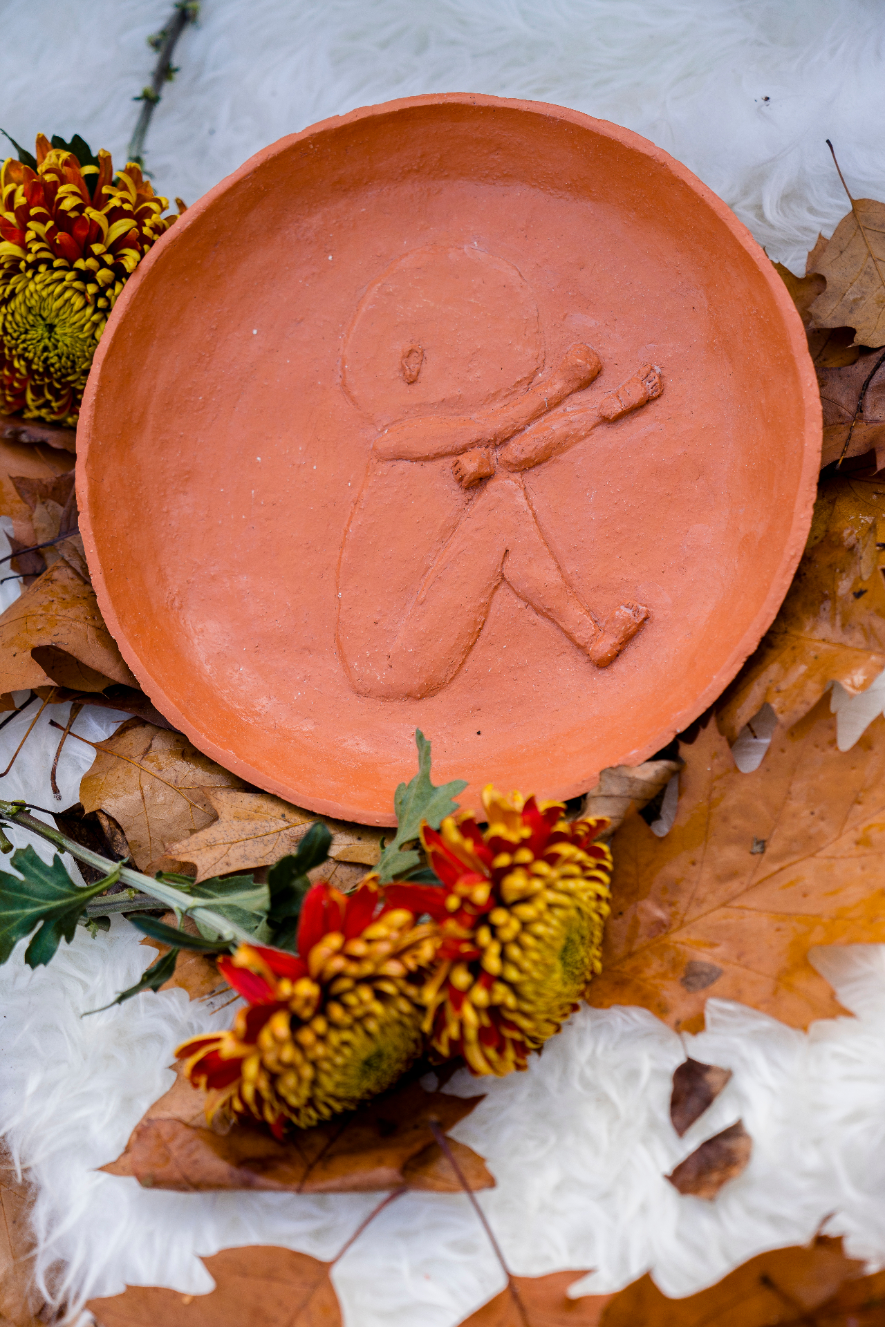 Handgemaakte terracotta schaal met de afdruk van een kindje, tussen herfstbladeren en chrysanten